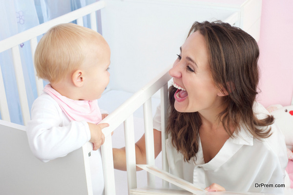 happy mother laughing with baby in crib