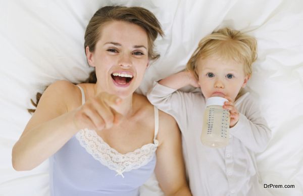 Mother laying with baby in bed and pointing in camera. Upper view