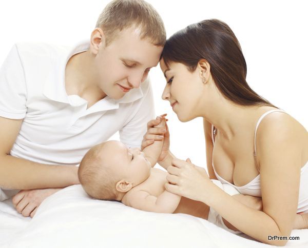 Happy young parents and baby lying on the bed
