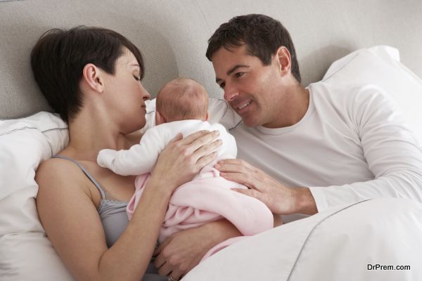 Parents Cuddling Newborn Baby In Bed At Home